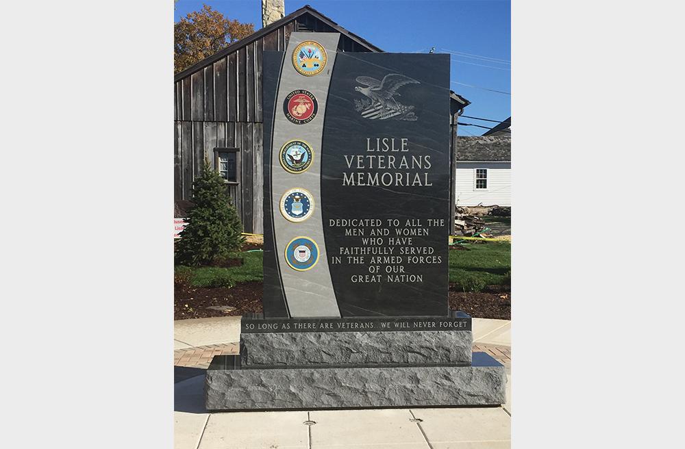 Veterans memorial made of grey granite with badges and atop pedestal